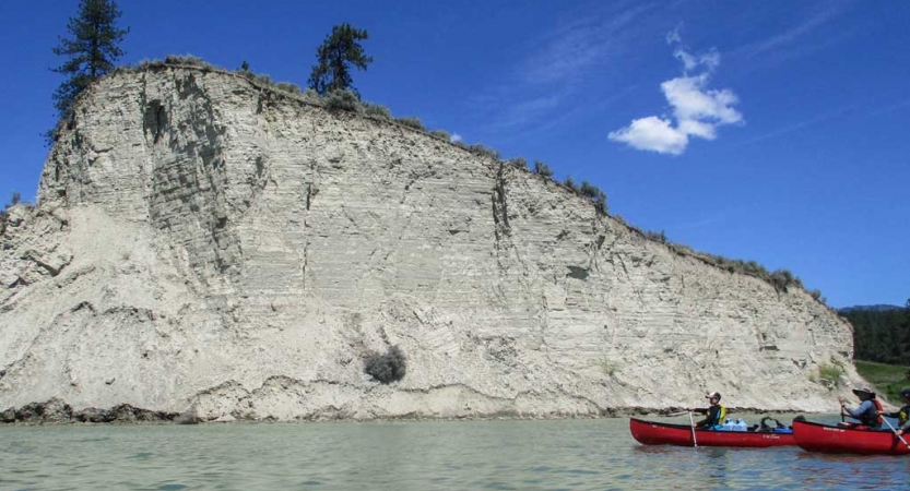 two canoes are paddled on calm water beside a tall white cliff